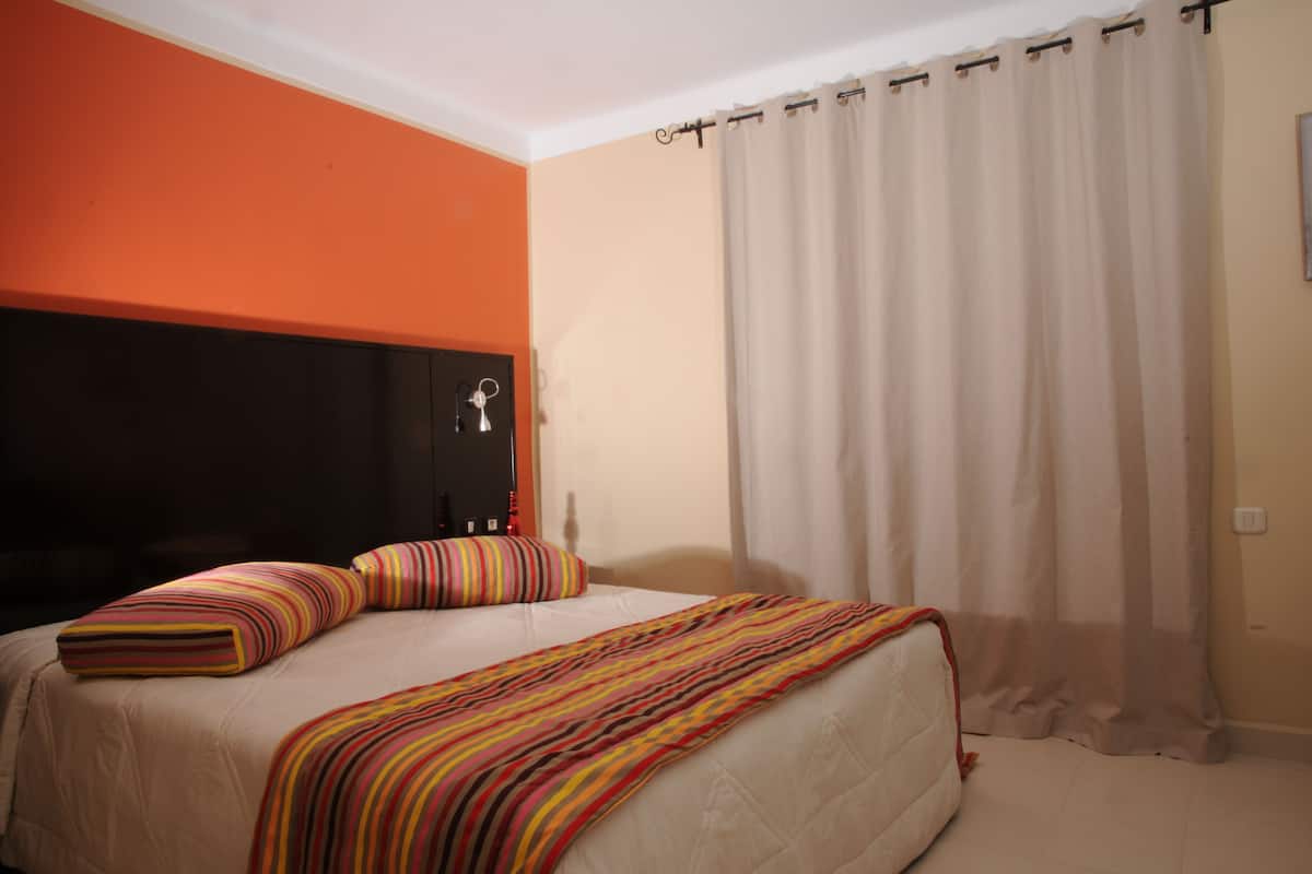 A bedroom with a bed, a headboard, a bedside table, and a curtain.