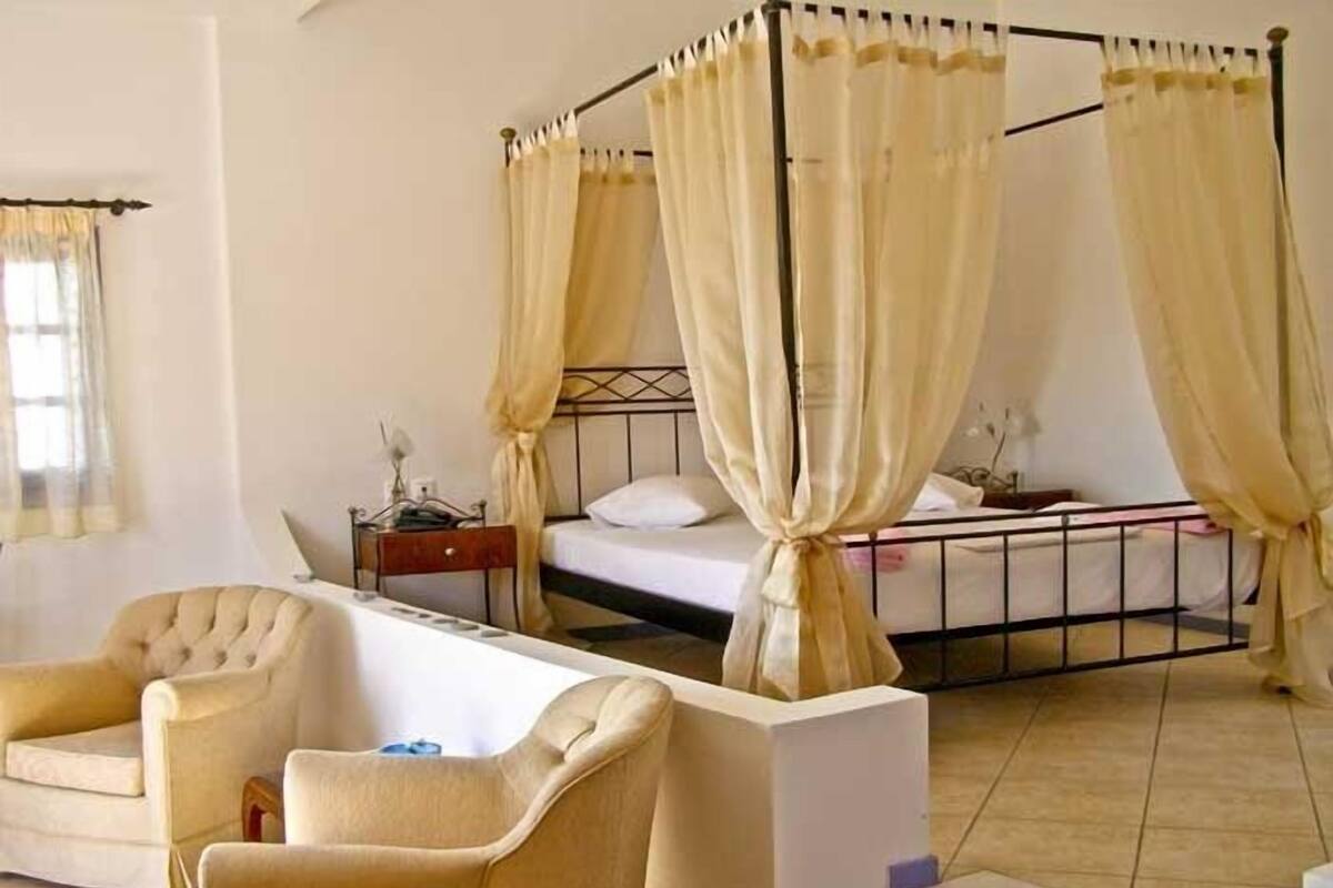A four-poster bed with curtains, a sofa, and a bedside table in a room with a tiled floor.
