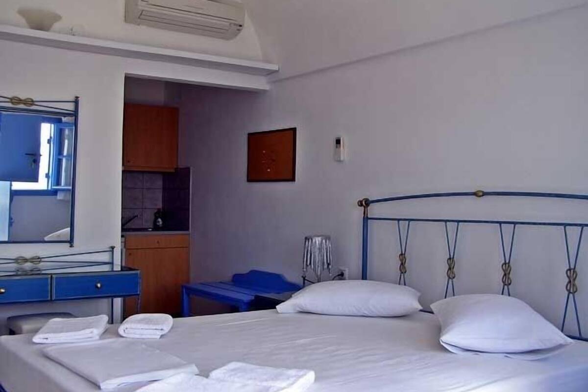 A hotel room with a bed, a desk, a mirror, and a small kitchenette.