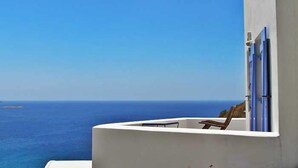 Un balcon donnant sur la mer, une chaise et un bâtiment à la façade blanche agrémentée de touches de bleu.