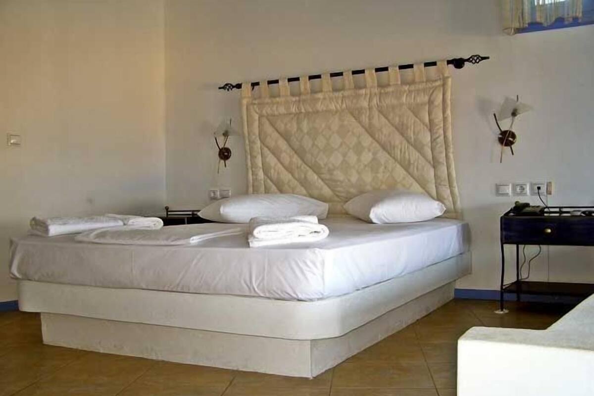 A neatly made bed with white linens and a quilted headboard, a bedside table with a lamp, and a wall-mounted decorative item.