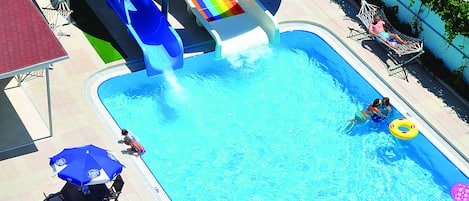 A water park with a multi-colored water slide, a swimming pool, and lounge chairs with umbrellas.