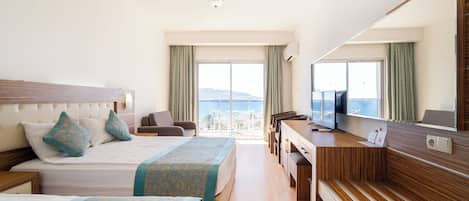 Una habitación de hotel con cama, escritorio, silla y un amplio ventanal con vista al mar.