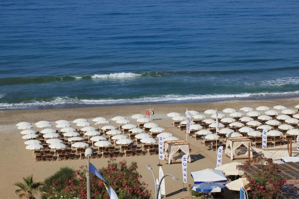 A beach with rows of umbrellas and lounge chairs, some with 'BEACH' signage, and a lifeguard tower in the background.