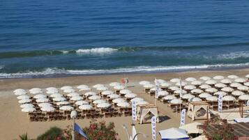 A beach with rows of umbrellas and lounge chairs, some with 'BEACH' signage, and a lifeguard tower in the background.