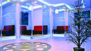 Um lobby moderno com divisórias de vidro, assentos vermelhos e uma árvore decorativa.