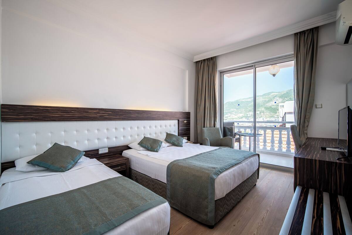 A hotel room with two beds, a TV, a desk, and a balcony with a view.