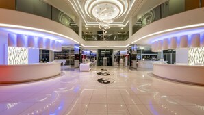 Un hall d’hôtel moderne avec un luminaire central en forme de spirale, un comptoir d’accueil et un sol épuré et réfléchissant.