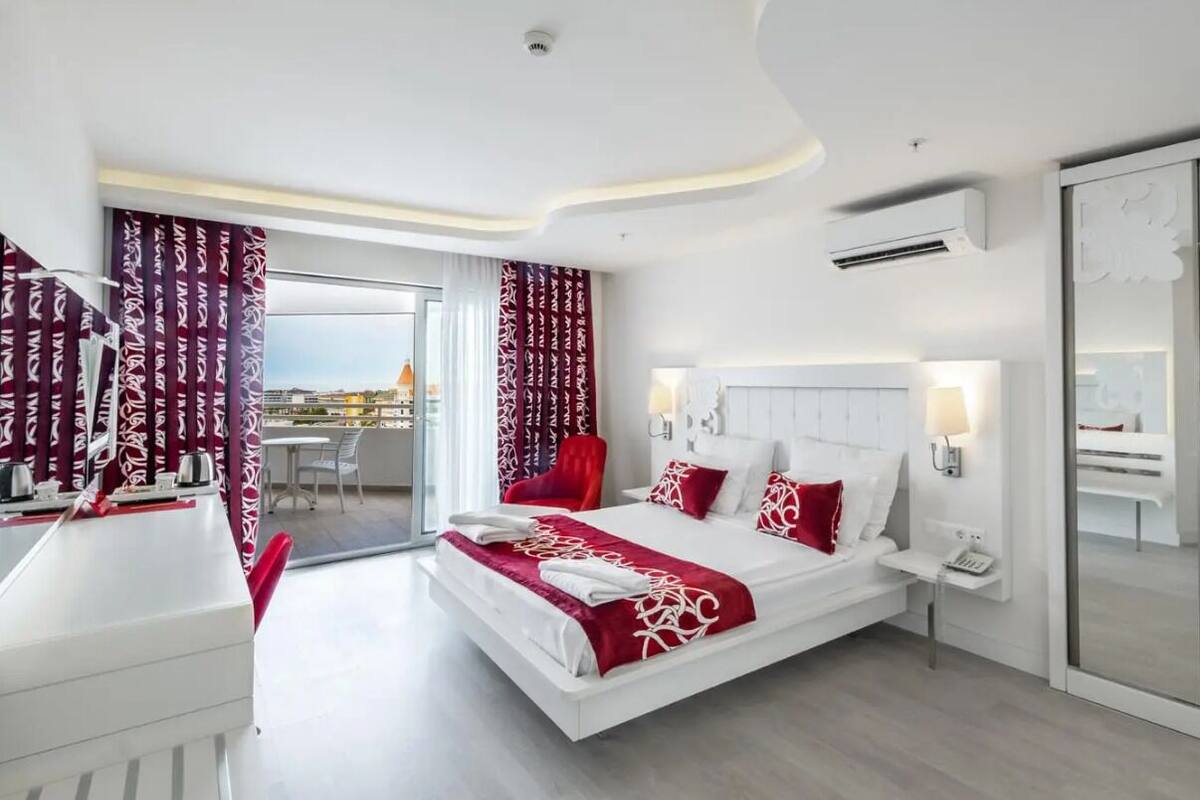 A modern hotel room with a large bed, a desk, and a balcony with a view.