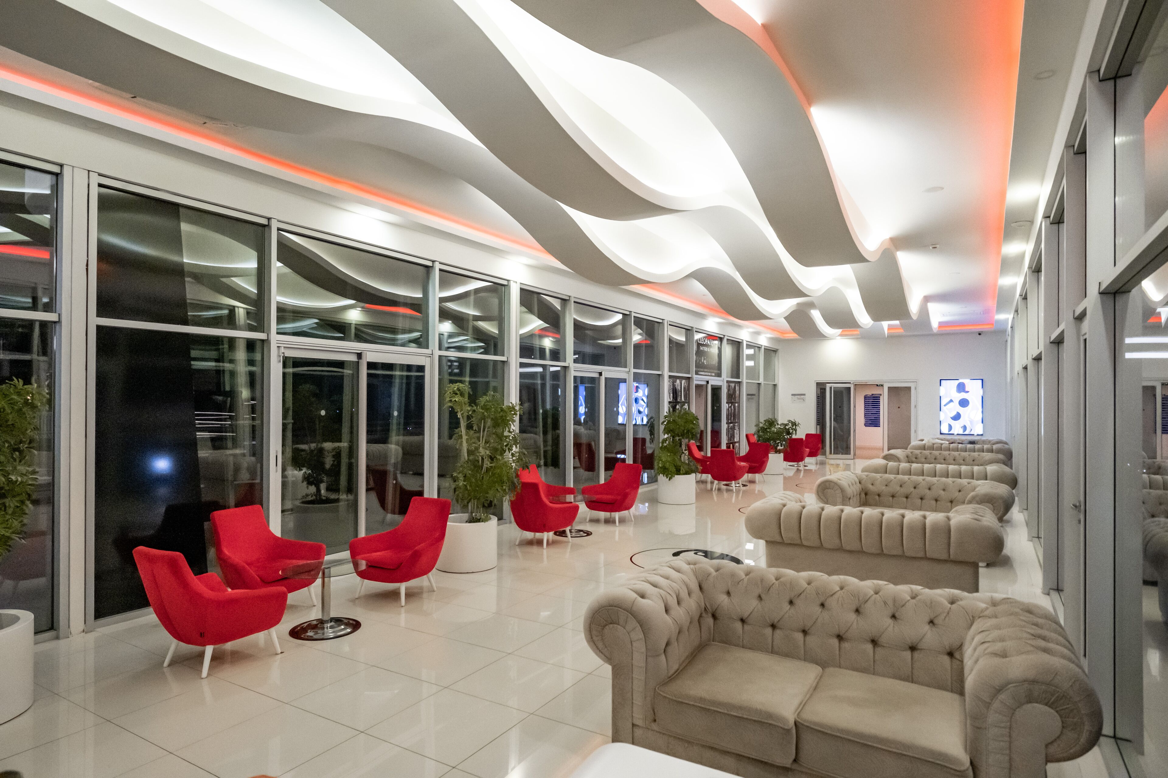 A modern lobby with curved ceiling lights, red and beige seating, and large windows.