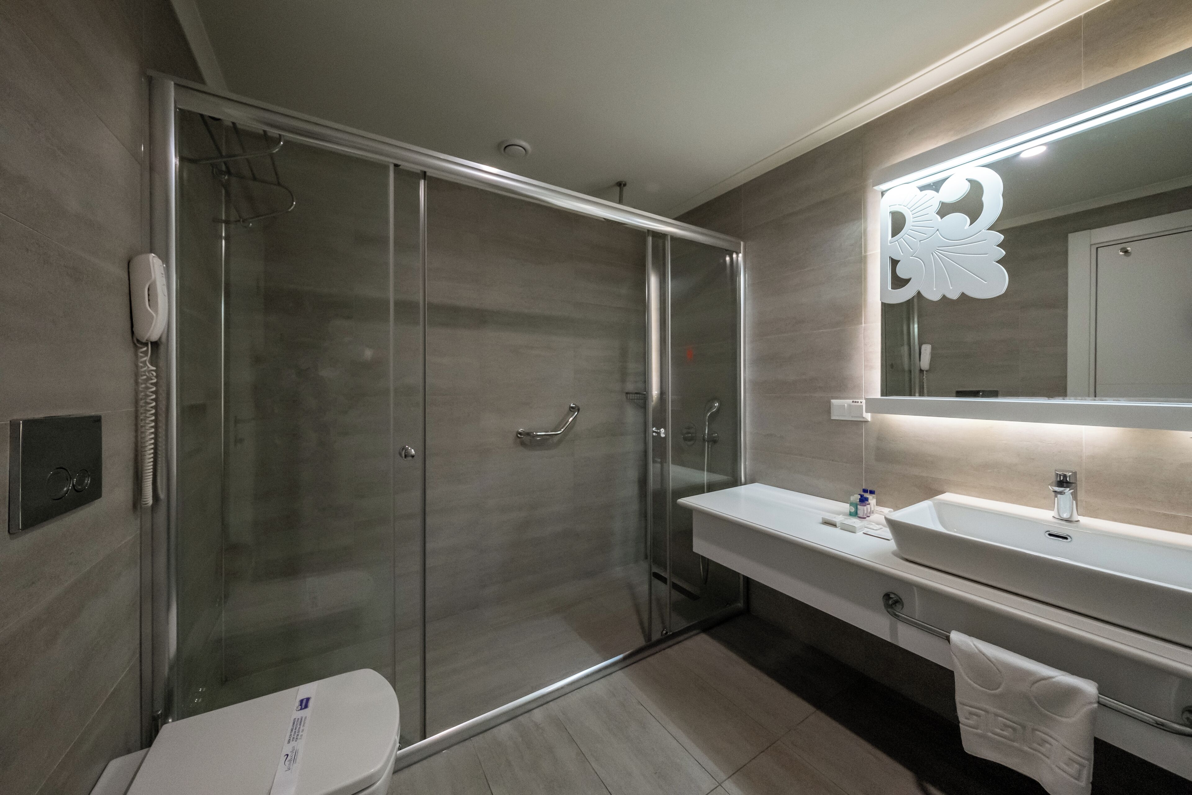 A modern bathroom with a glass-enclosed shower, a white sink, and a large mirror with a decorative light fixture above it.