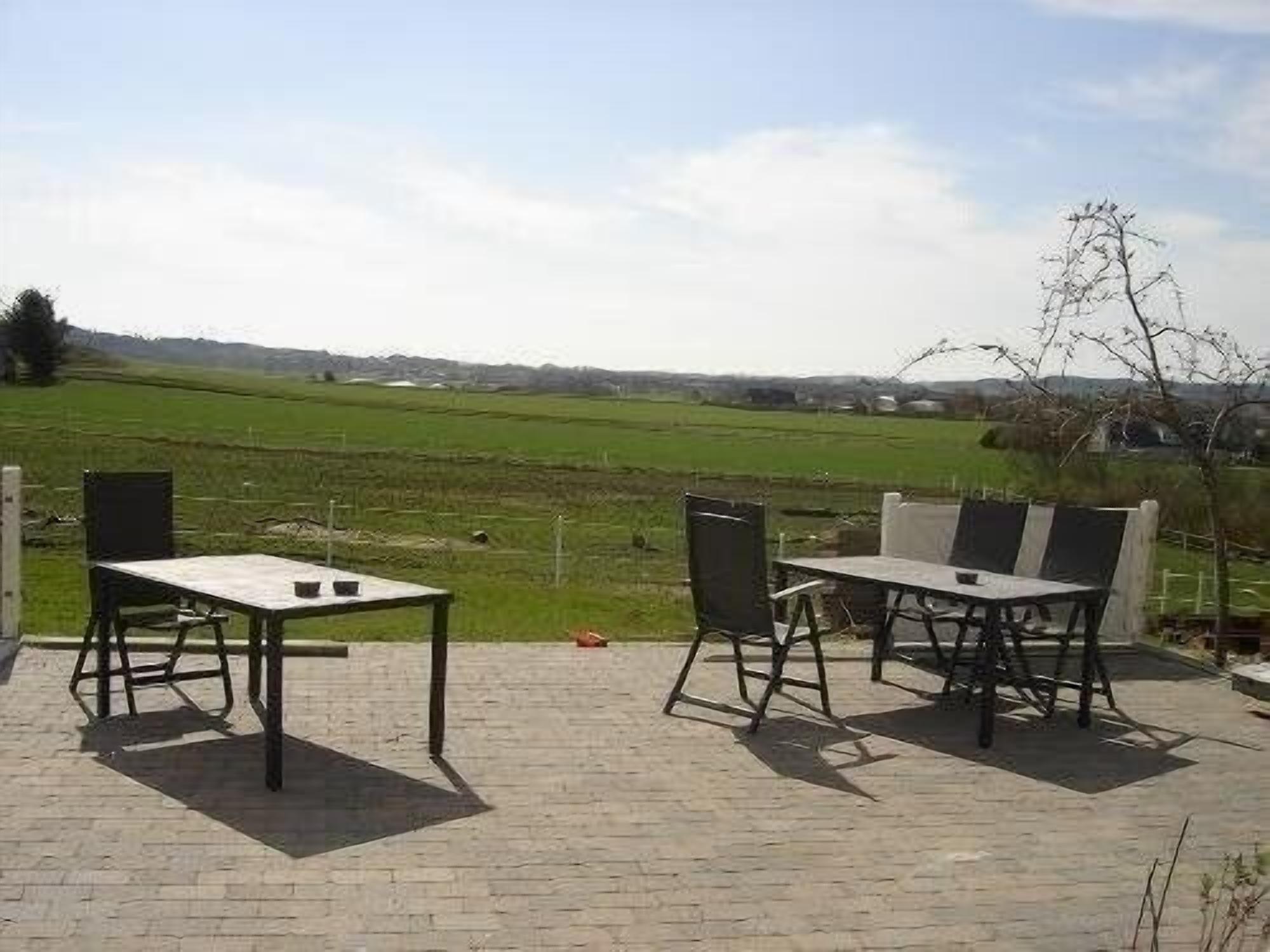 An outdoor patio with two tables and chairs, a brick floor, and a view of a green field and distant hills.