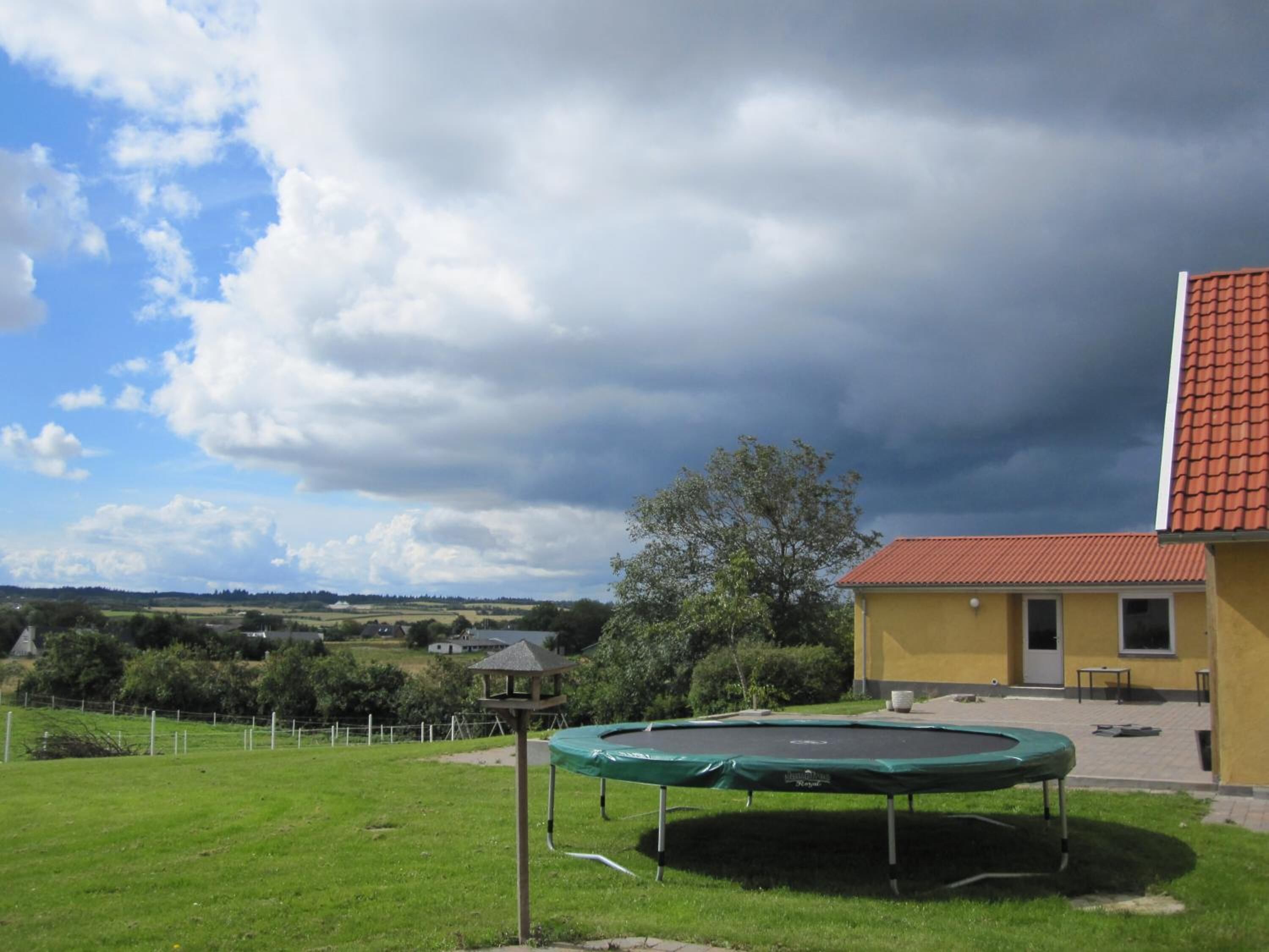 A trampoline in a grassy yard with a yellow building in the background.