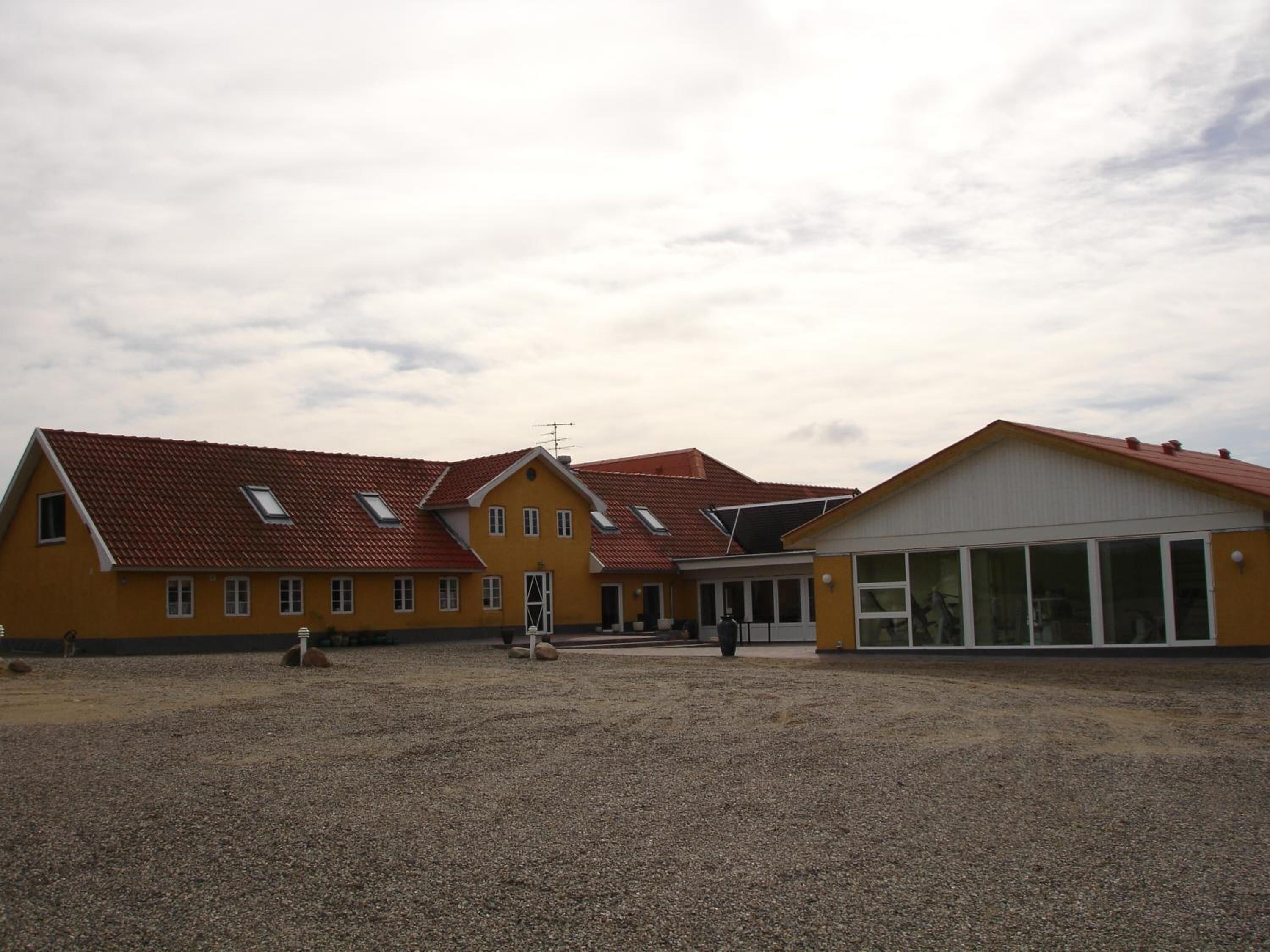 A yellow building with a red roof, a covered entrance, and a gravel courtyard.