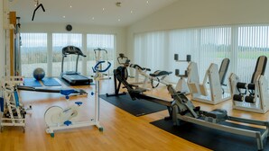 A spacious gym with various exercise equipment, large windows, and a wooden floor. - Hotel Højgaarden (Fjerritslev)