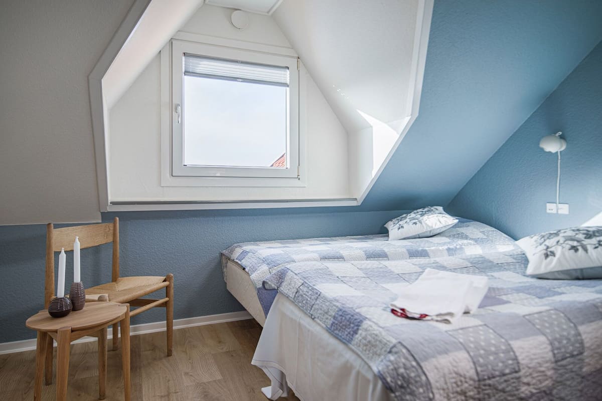 A bedroom with a sloped ceiling, a single bed, a wooden chair, and a small table with candles.