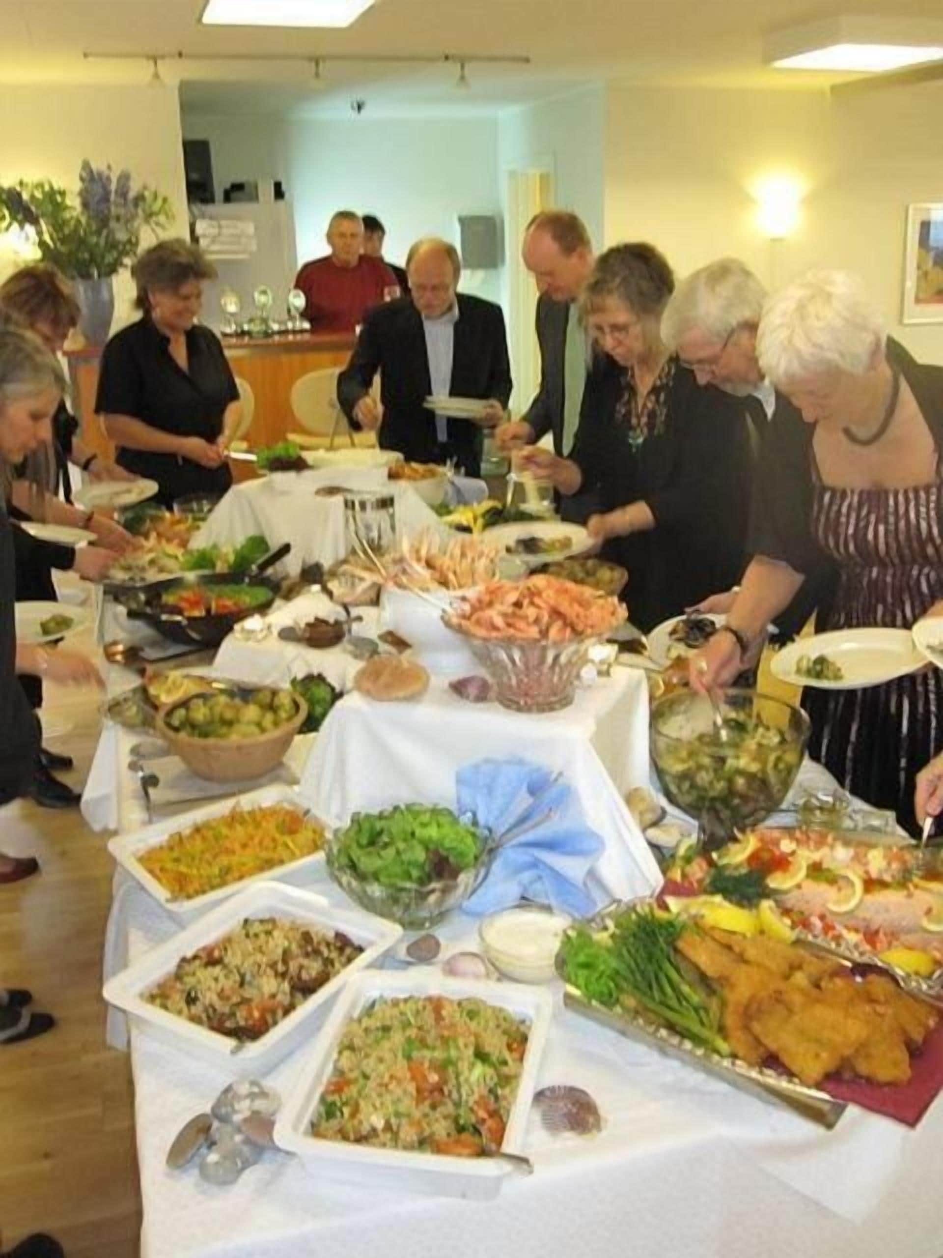 Une table de buffet proposant divers plats, et un groupe de personnes se servant elles-mêmes.