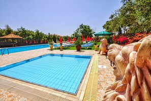 A swimming pool with a tiled deck, surrounded by lounge chairs and umbrellas, and a decorative lion statue. - Hadjios Valley (Mazotos)