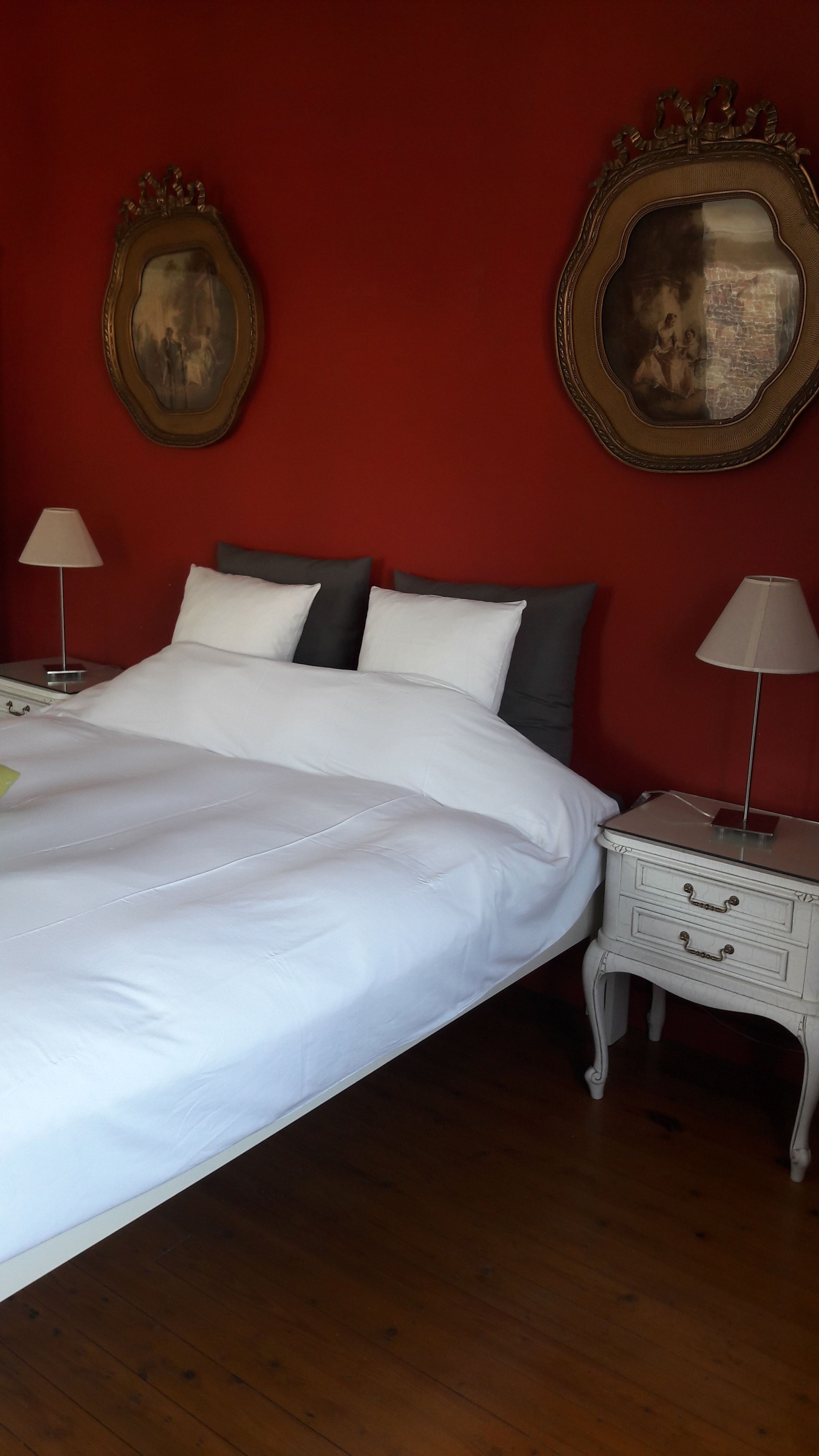 A neatly made bed with white linens, two pillows, and a nightstand with a lamp. There are two framed pictures on the wall.