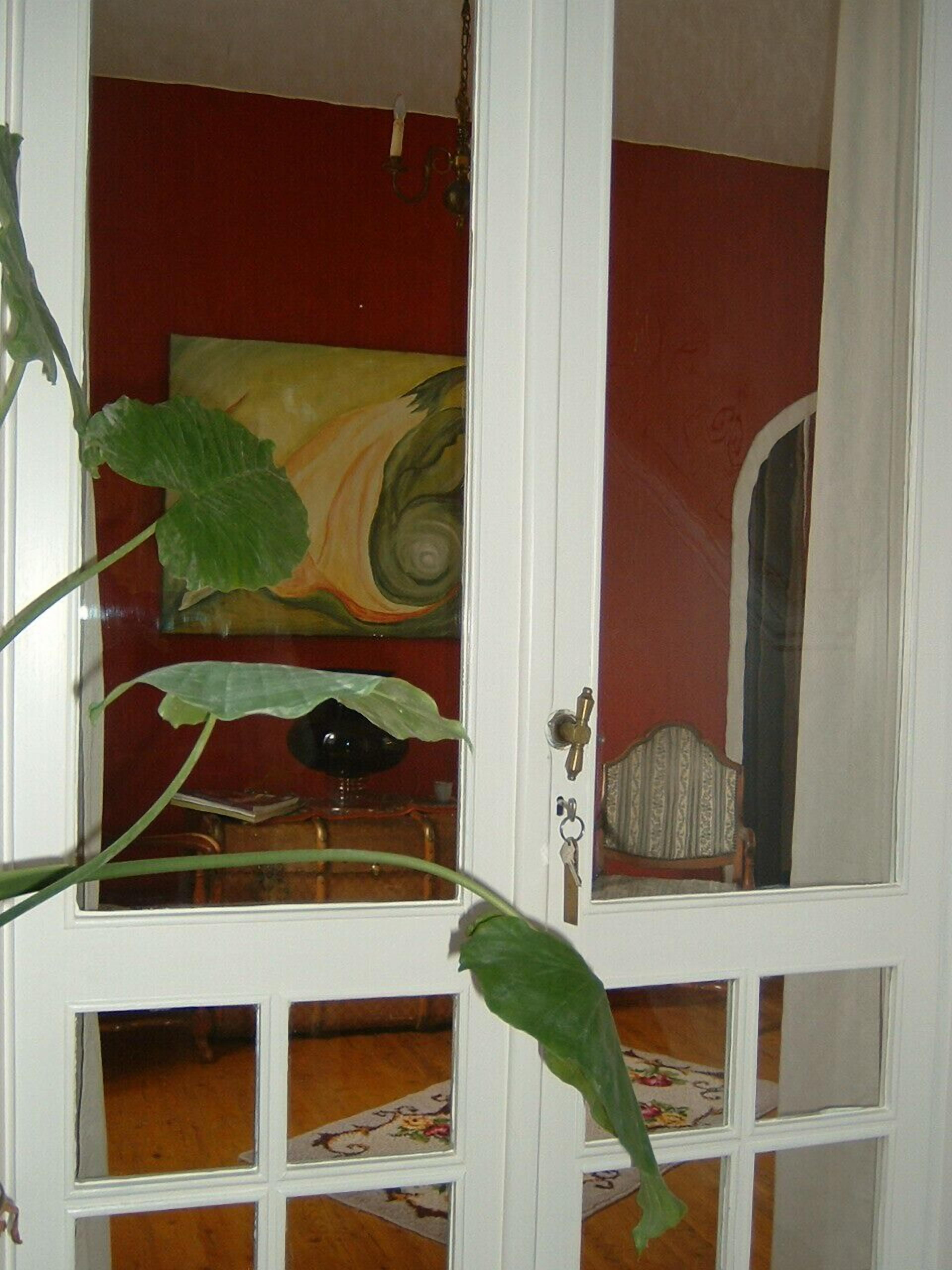 Quarto com parede vermelha, porta branca com painéis de vidro e uma grande planta verde em primeiro plano.