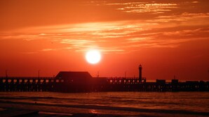 A sunset over a pier with a lighthouse and buildings in silhouette. - B&B Villa D'Hondt (Blankenberge)