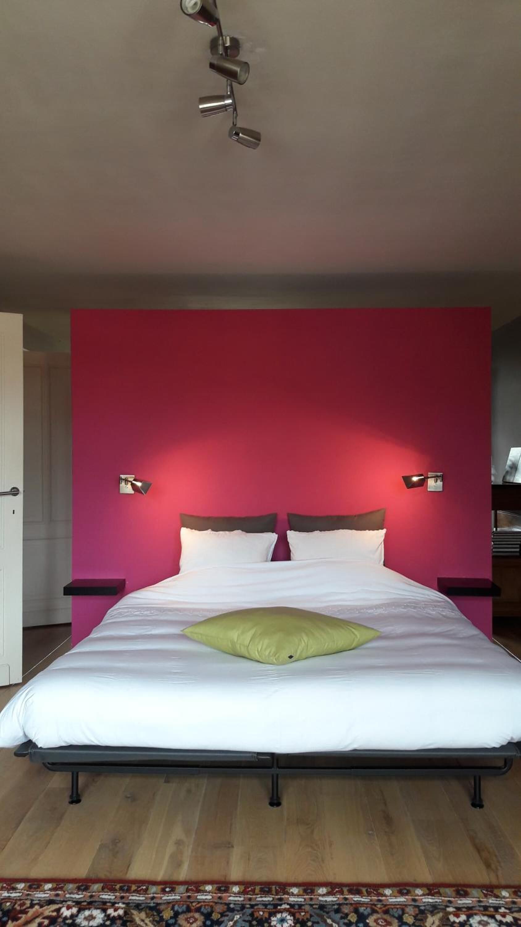 Ein Schlafzimmer mit einem Bett, einer roten Wand, zwei Nachttischlampen und einem gemusterten Teppich.