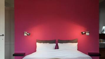 Ein Schlafzimmer mit einem Bett, einer roten Wand, zwei Nachttischlampen und einem gemusterten Teppich.