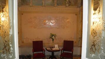 Een kamer met twee rode stoelen, een tafeltje met een bloevas en een decoratieve wand met een centraal embleem.