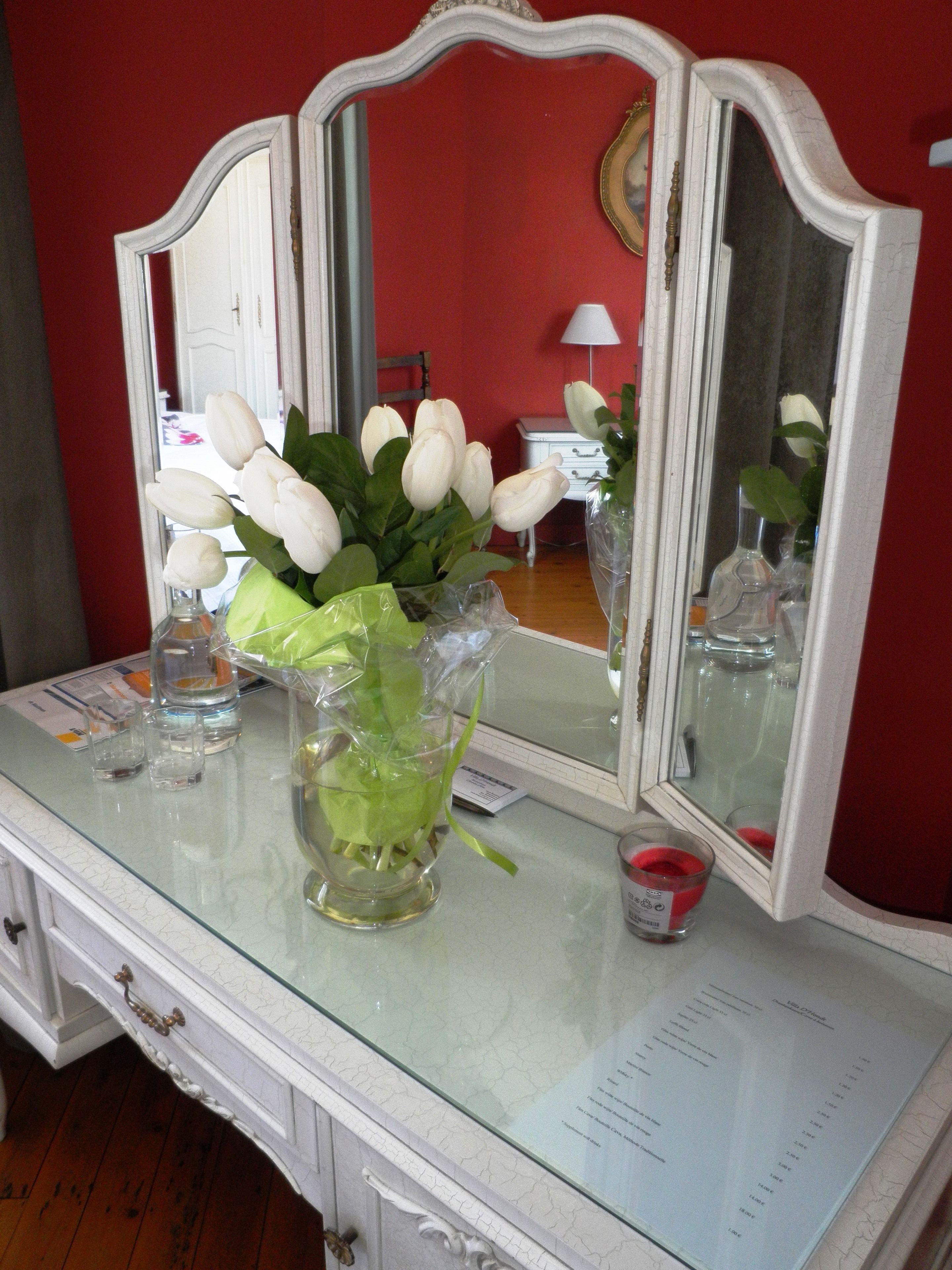 Un mobile toilette con specchio, un vaso con fiori bianchi e una piccola candela.