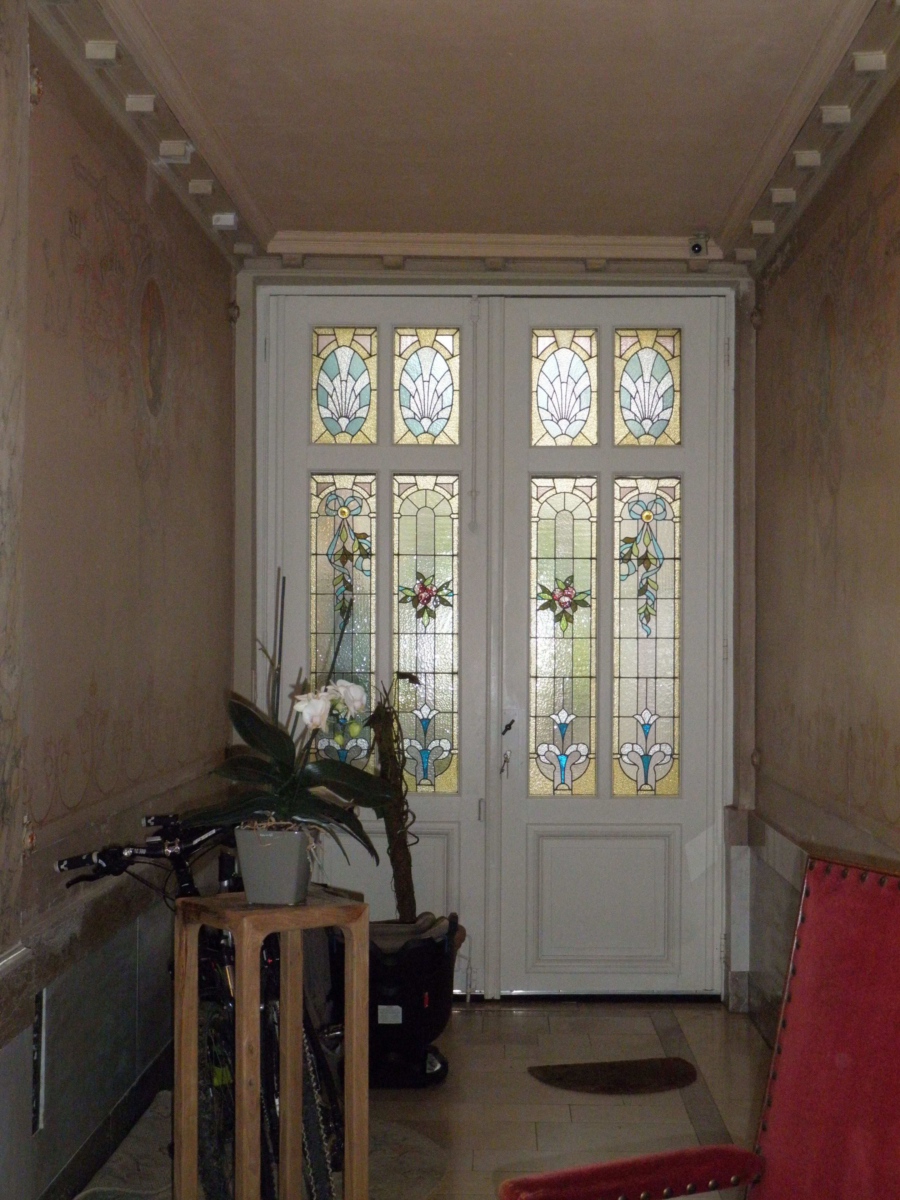 A room with a white door featuring stained glass windows, a potted plant, and a wooden chair.