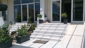 A building entrance with a set of stairs leading up to a door, potted plants, and a welcome mat. - Porto Marathos (Trifylia)