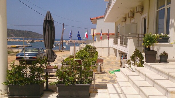A balcony with potted plants, a car, and flags. - Porto Marathos (Trifylia)