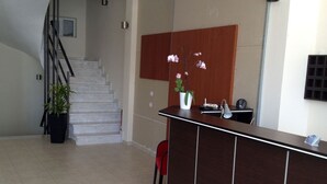 A reception area with a wooden desk, a potted plant, a red chair, and a staircase in the background. - Porto Marathos (Trifylia)