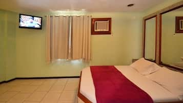 Quarto de hotel com cama, televisão, janela com cortinas e espelho.