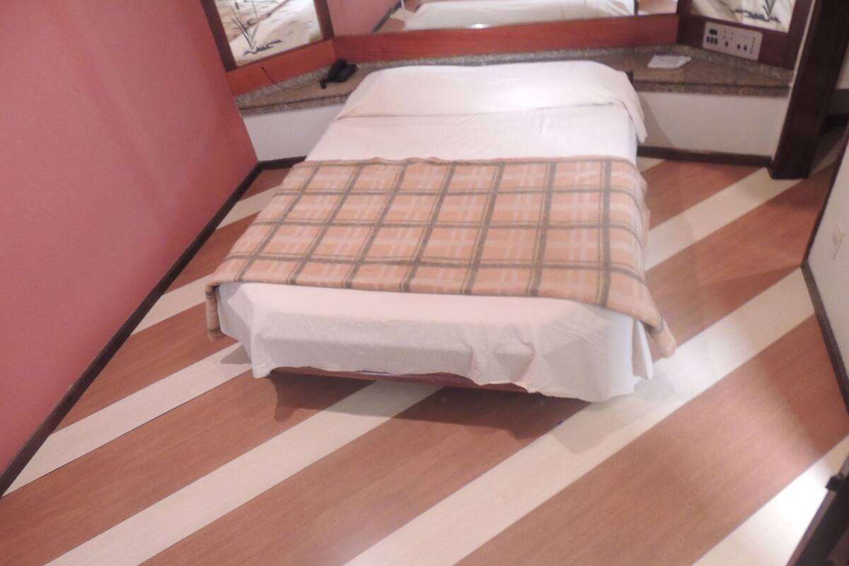 Una cama individual con una manta de cuadros en una habitación con piso a rayas y una pared roja.