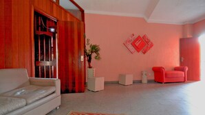 A living room with a beige sofa, a red chair, a wooden door, and a pink wall with two red decorative items. - Verona Hotel - Adults Only (Rio de Janeiro)
