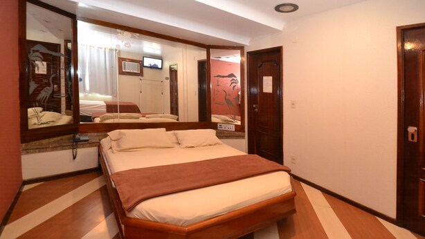 A hotel room with a large bed, a wooden floor, a mirror, and a door. - Verona Hotel - Adults Only (Rio de Janeiro)