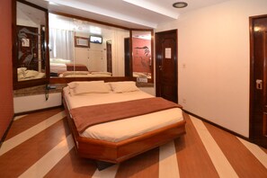 Une chambre d’hôtel avec un grand lit, un plancher en bois, un miroir et une porte.