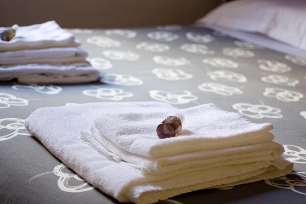 A neatly folded stack of white towels on a bed with a floral pattern bedspread. - Luci a San Siro (Milan)