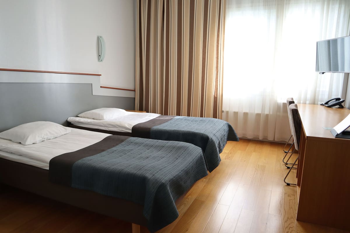 Ein Hotelzimmer mit zwei Betten, einem Schreibtisch mit Telefon und einem an der Wand befestigten Fernseher.
