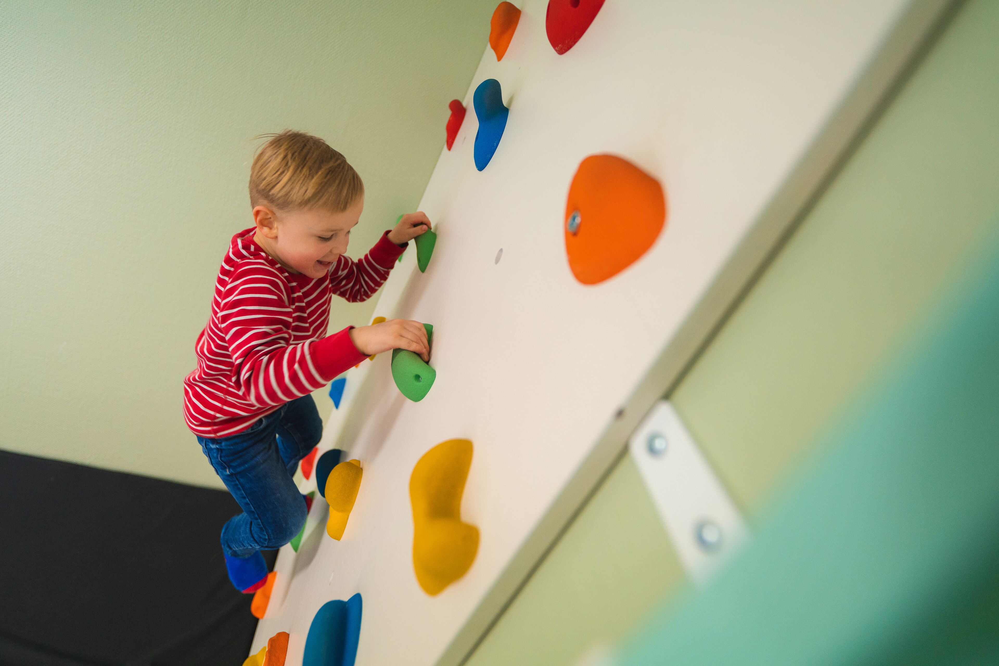 A child climbing a wall with colorful handholds.