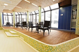 A spacious indoor area with a wooden floor, tiled walls, and large windows.