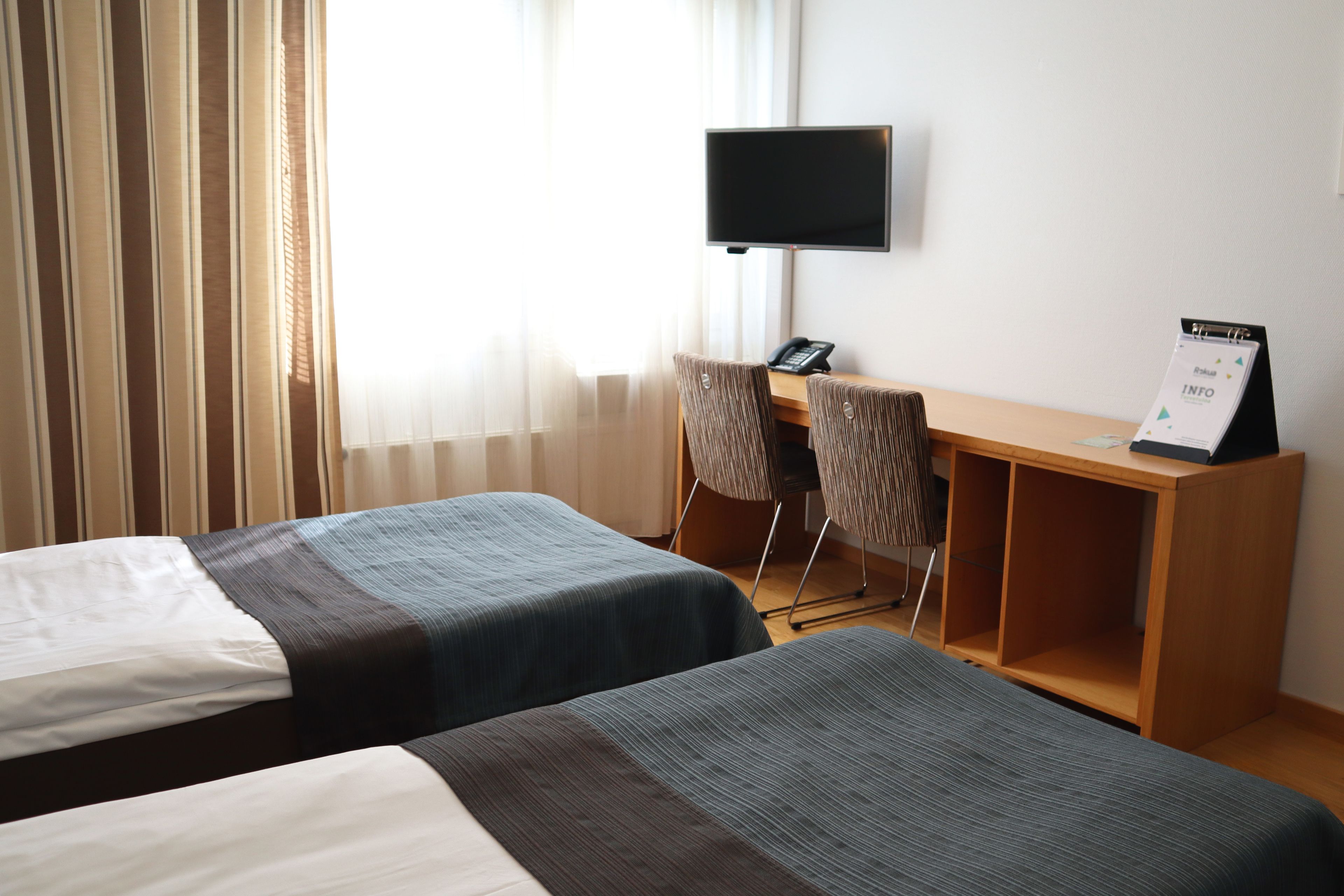A hotel room with two beds, a desk with a chair, a television, and a signboard.