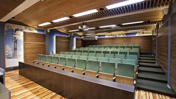 A lecture hall with rows of green chairs, wooden paneling on the walls, and a wooden floor.