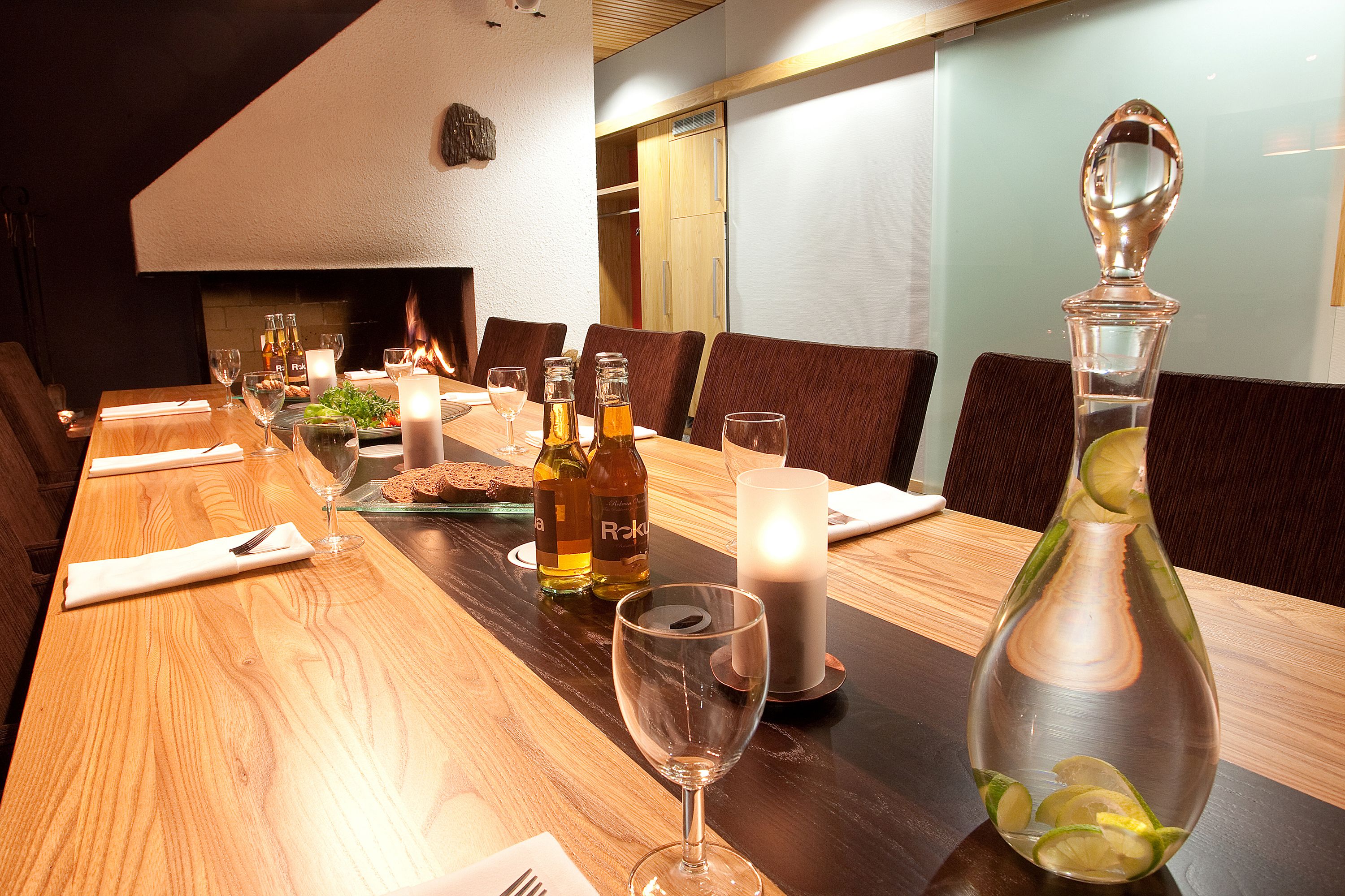 A dining table set for six with candles, wine glasses, and a bottle of liquor.