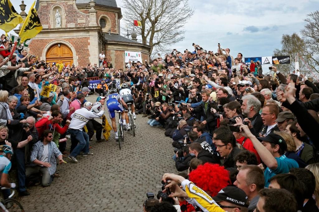 A crowd of people gathered around a cyclist in a cobblestone street.