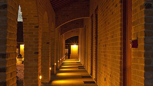 A corridor with brick walls and a wooden ceiling, leading to a door at the end.