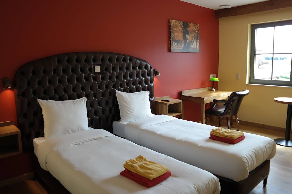 Ett hotellrum med två sängar, ett skrivbord, en stol och ett fönster.