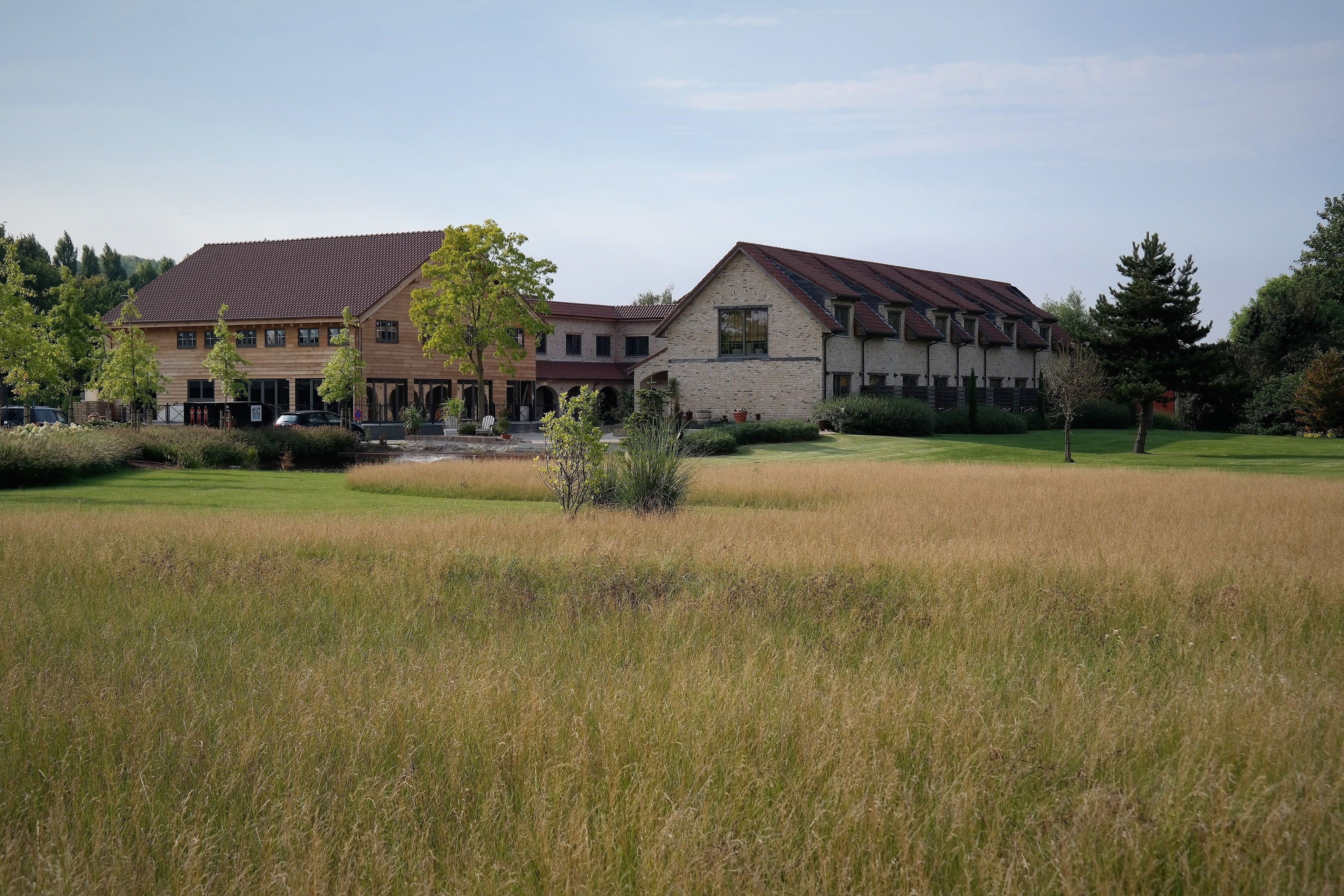 A building with a red roof and stone facade, surrounded by a well-maintained lawn and trees.