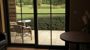 A room with a large sliding glass door leading to an outdoor patio area with a table and chairs, a view of a landscaped garden, and a pond.